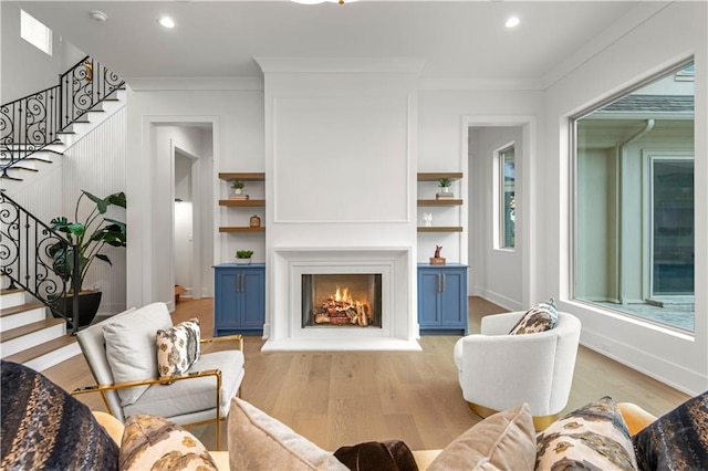 living room with light wood finished floors, a warm lit fireplace, crown molding, and stairs