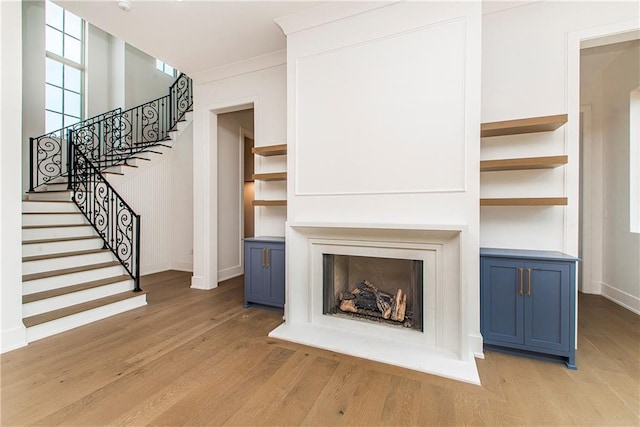 unfurnished living room featuring light wood-style flooring, a fireplace, crown molding, baseboards, and stairs