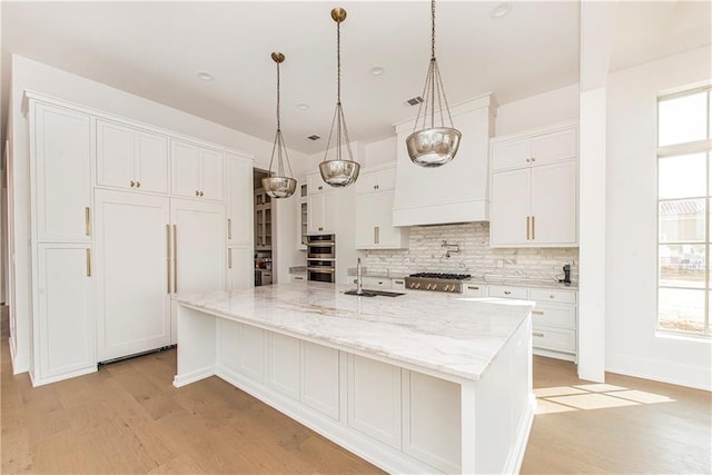 kitchen with a spacious island, a sink, decorative backsplash, white cabinets, and light wood-style floors