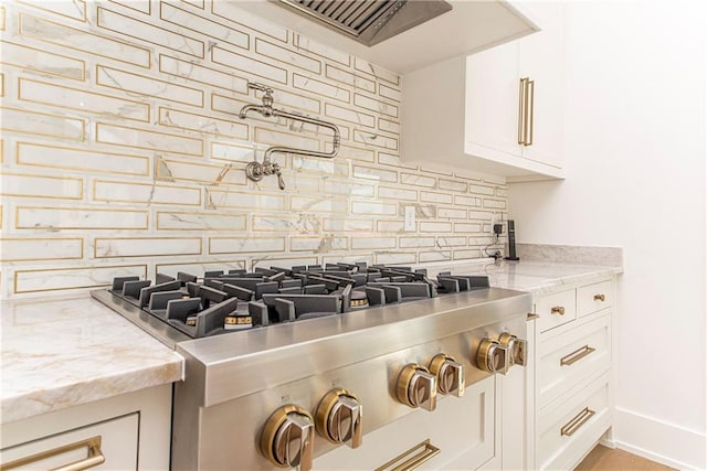 interior details with tasteful backsplash, baseboards, light stone counters, stainless steel gas stovetop, and white cabinets