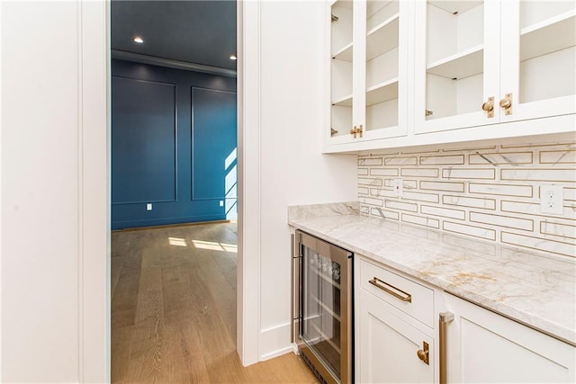 bar with light wood-type flooring, decorative backsplash, a bar, and beverage cooler