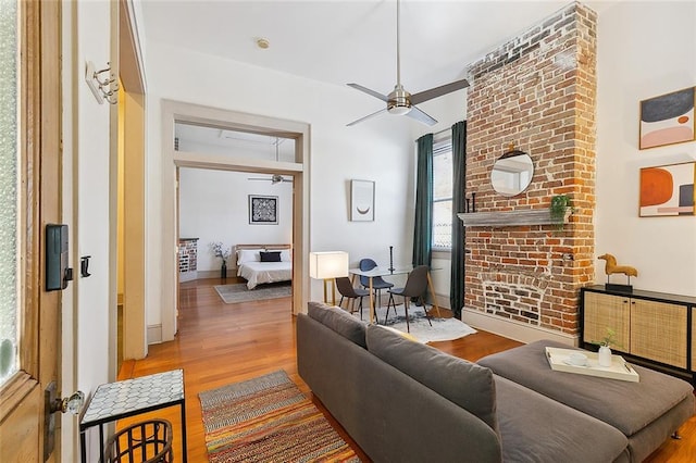 living area featuring baseboards, ceiling fan, wood finished floors, and a fireplace