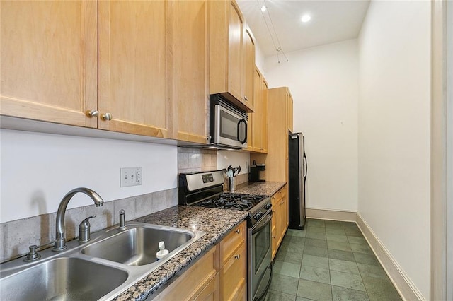 kitchen featuring dark countertops, a sink, light brown cabinets, stainless steel appliances, and baseboards