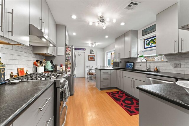 kitchen featuring gray cabinets, under cabinet range hood, a sink, dark countertops, and appliances with stainless steel finishes