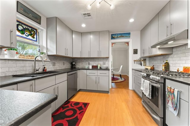 kitchen featuring dark countertops, visible vents, under cabinet range hood, light wood-style flooring, and appliances with stainless steel finishes