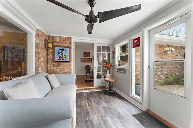 interior space featuring wood finished floors, a ceiling fan, baseboards, brick wall, and crown molding