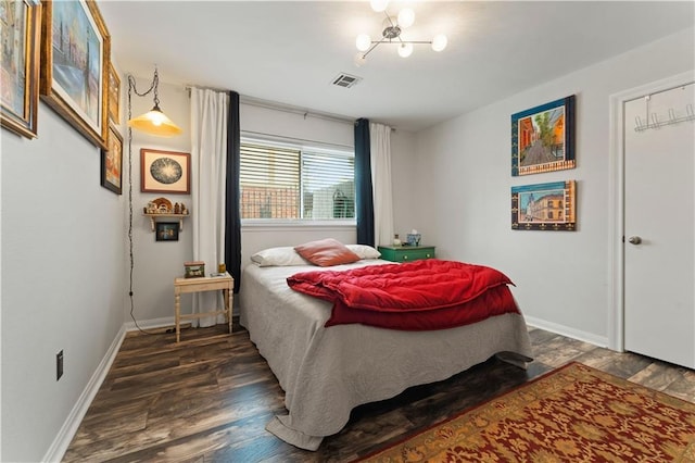 bedroom featuring a notable chandelier, visible vents, baseboards, and wood finished floors