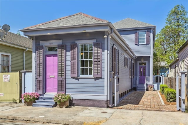 shotgun-style home featuring roof with shingles and fence