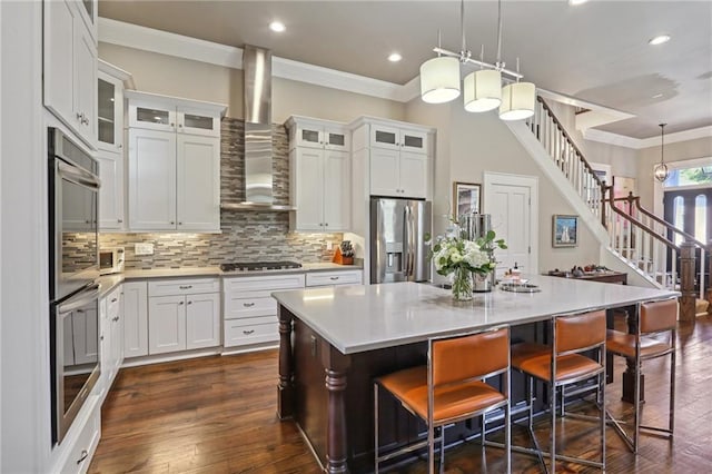 kitchen with light countertops, wall chimney exhaust hood, stainless steel fridge with ice dispenser, and ornamental molding