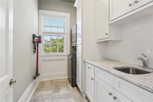 kitchen featuring baseboards, light stone countertops, decorative backsplash, white cabinetry, and a sink