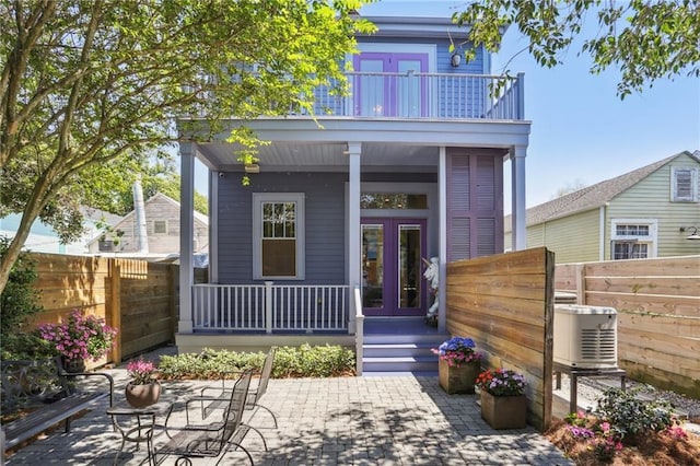 rear view of house featuring french doors, a balcony, a porch, and fence