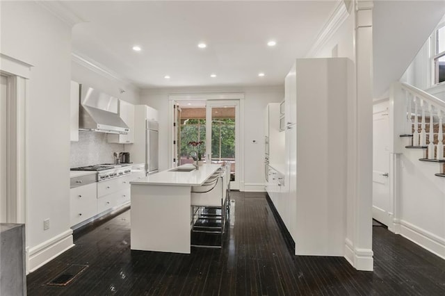 kitchen featuring crown molding, wall chimney range hood, appliances with stainless steel finishes, white cabinetry, and a sink