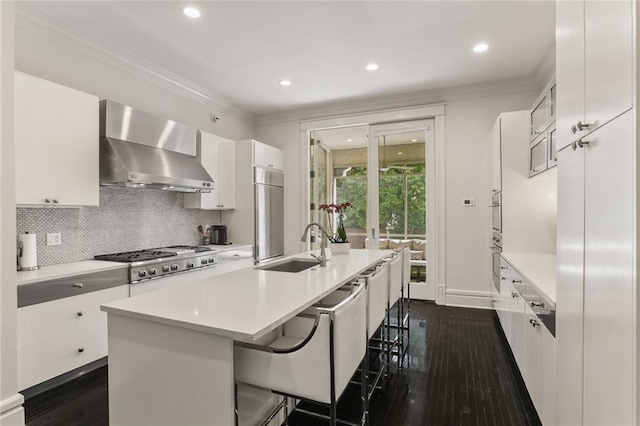 kitchen featuring a sink, white cabinets, crown molding, wall chimney range hood, and backsplash