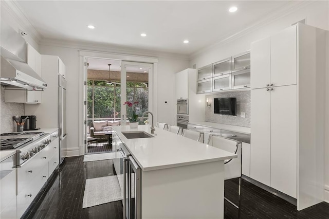 kitchen featuring an island with sink, stainless steel appliances, a sink, light countertops, and crown molding