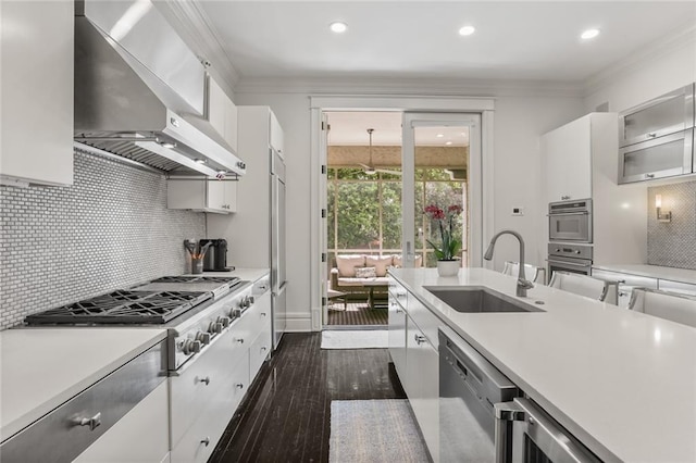 kitchen with light countertops, crown molding, wall chimney range hood, and a sink