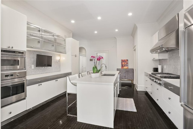 kitchen with dark wood-style floors, a center island with sink, ornamental molding, stainless steel appliances, and a sink