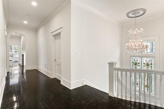 hall with dark wood finished floors, crown molding, an upstairs landing, and arched walkways