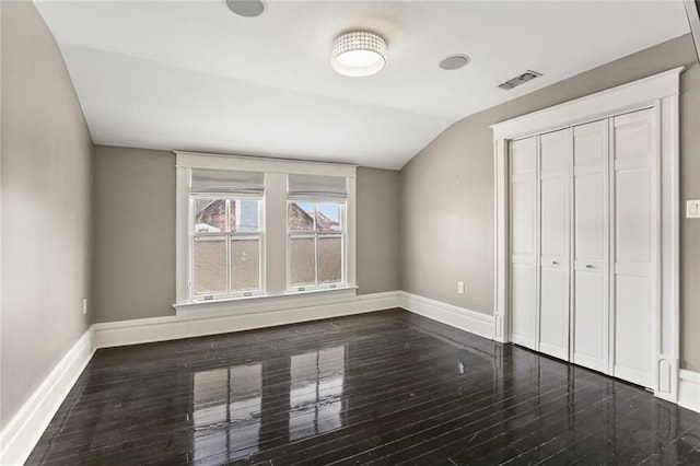 unfurnished bedroom featuring visible vents, wood finished floors, a closet, baseboards, and vaulted ceiling