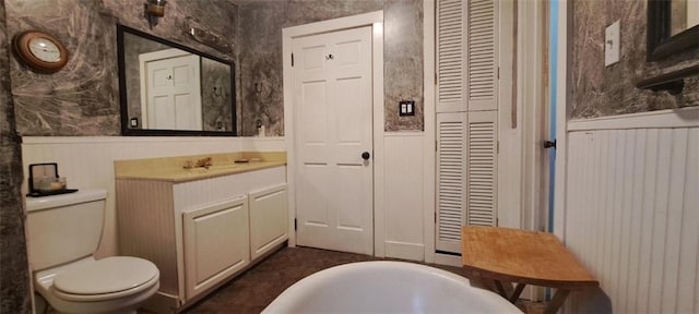 bathroom featuring a closet, toilet, wainscoting, and wallpapered walls