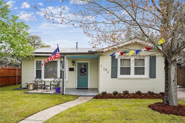 bungalow-style home featuring brick siding, roof mounted solar panels, a front lawn, and fence