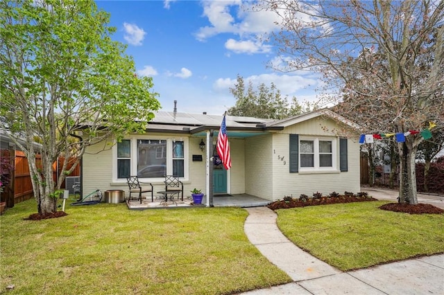 view of front of house with a front yard, fence, brick siding, and roof mounted solar panels