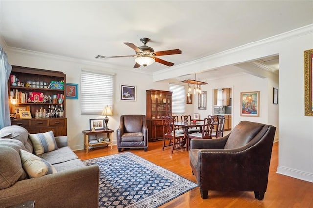 living area with visible vents, ornamental molding, ceiling fan with notable chandelier, wood finished floors, and baseboards