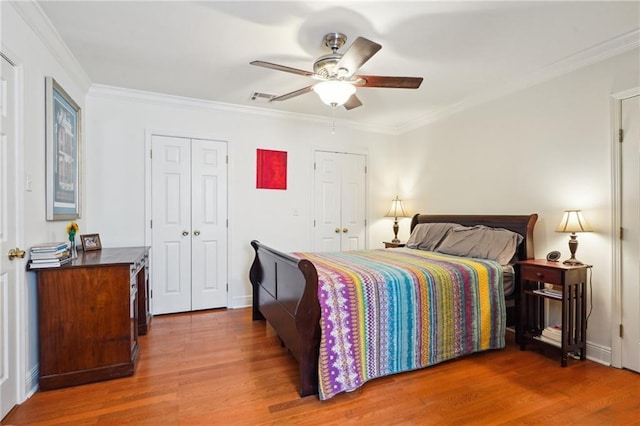 bedroom featuring visible vents, multiple closets, ornamental molding, a ceiling fan, and wood finished floors