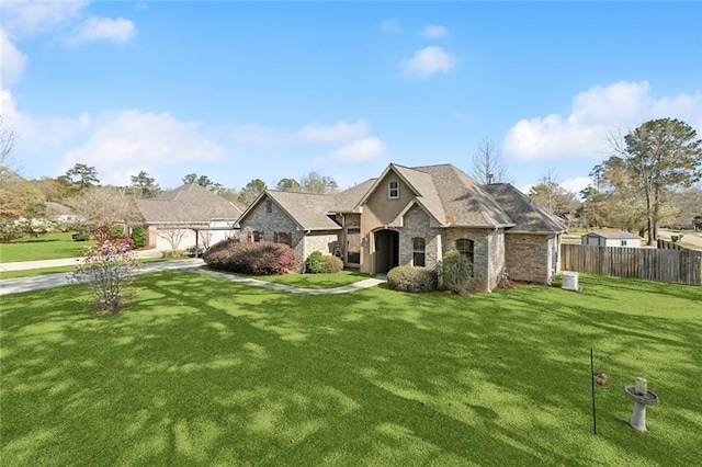 french provincial home featuring fence, driveway, an attached garage, a front lawn, and stone siding