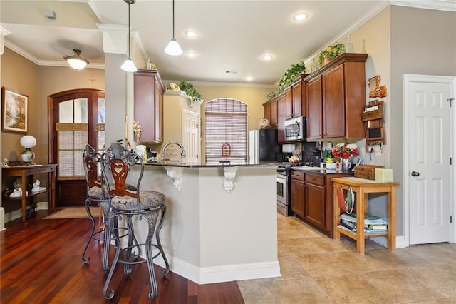 kitchen with a breakfast bar, a peninsula, appliances with stainless steel finishes, crown molding, and hanging light fixtures