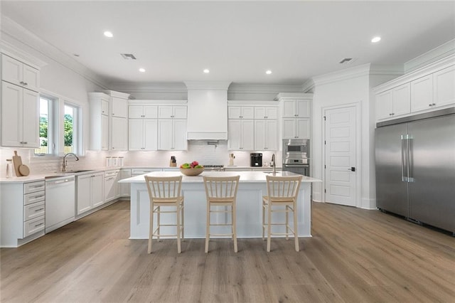 11 Khan Ct, Metairie, LA 70003 - kitchen featuring built in appliances, ornamental molding, light wood-style floors, decorative backsplash, and a kitchen island with sink