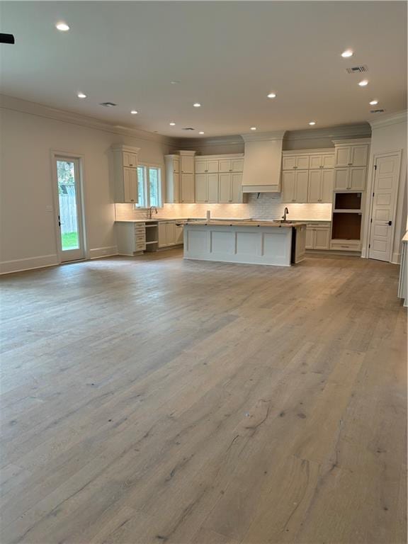 kitchen featuring custom exhaust hood, light wood-style flooring, backsplash, visible vents, and ornamental molding