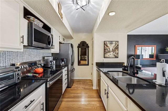 kitchen featuring light wood finished floors, a sink, appliances with stainless steel finishes, white cabinetry, and backsplash