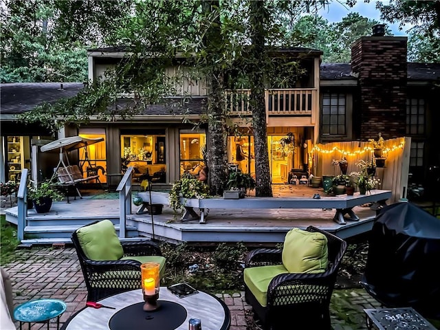 rear view of property with a deck, a patio, roof with shingles, and a chimney