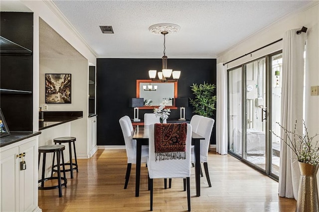 dining room featuring visible vents, ornamental molding, a textured ceiling, light wood-style floors, and an inviting chandelier