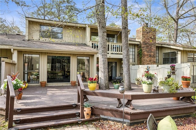 rear view of house featuring a balcony, board and batten siding, a chimney, and a deck