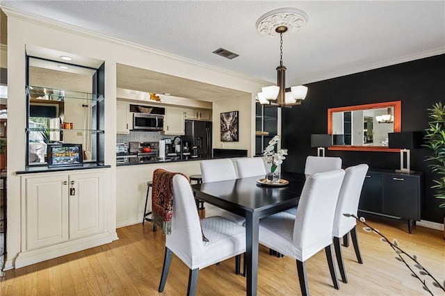 dining space featuring visible vents, ornamental molding, light wood-style flooring, a notable chandelier, and a textured ceiling