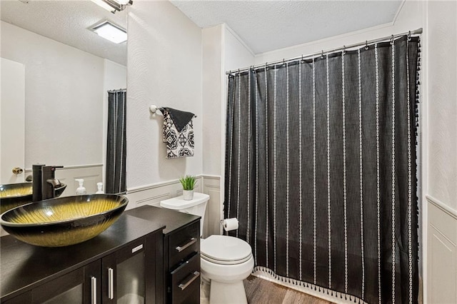 bathroom with a wainscoted wall, toilet, a textured ceiling, wood finished floors, and vanity