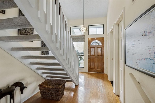 entrance foyer with light wood-type flooring, a textured ceiling, a high ceiling, and stairs