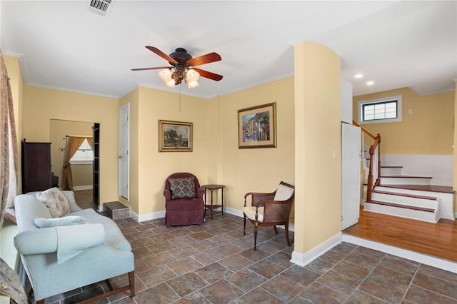 living area with a ceiling fan, visible vents, baseboards, stairs, and crown molding