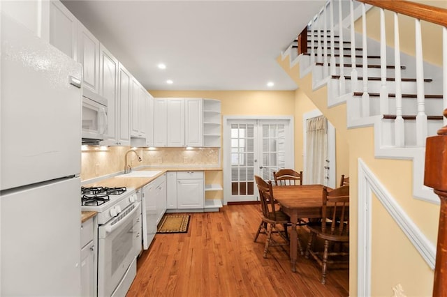 kitchen with light wood finished floors, open shelves, light countertops, white appliances, and a sink