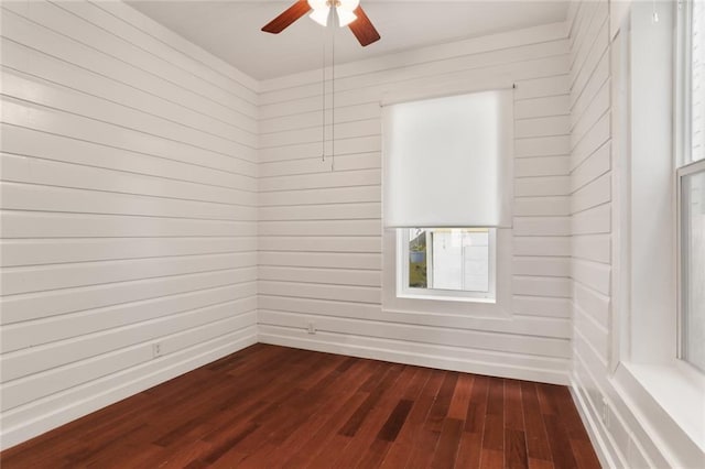 spare room featuring dark wood-type flooring, ceiling fan, and wooden walls