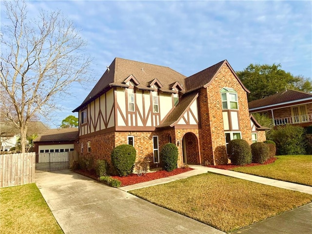 english style home with a front lawn, fence, roof with shingles, concrete driveway, and brick siding