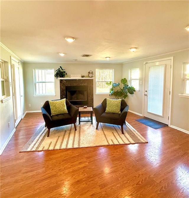 living area with a high end fireplace, visible vents, ornamental molding, and wood finished floors