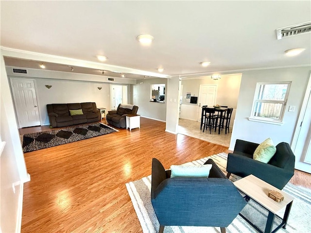 living area with visible vents, light wood-style flooring, and crown molding