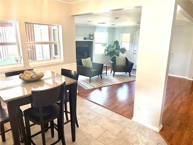 dining room with a fireplace, light wood-style floors, baseboards, and ornamental molding