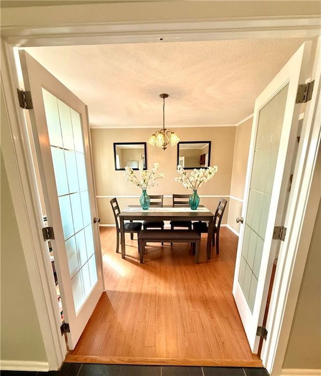 dining area with baseboards, a textured ceiling, crown molding, light wood-type flooring, and a chandelier