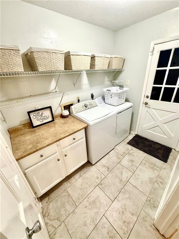 laundry area with washer and clothes dryer, light tile patterned floors, cabinet space, and a textured ceiling