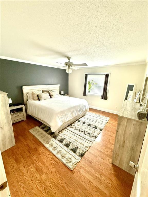 bedroom with a textured ceiling, a ceiling fan, baseboards, and wood finished floors