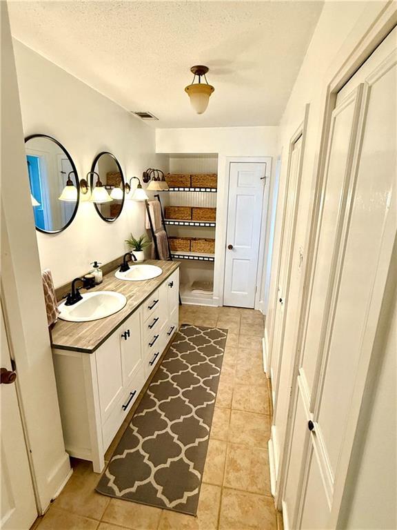 full bathroom with double vanity, tile patterned floors, a textured ceiling, and a sink