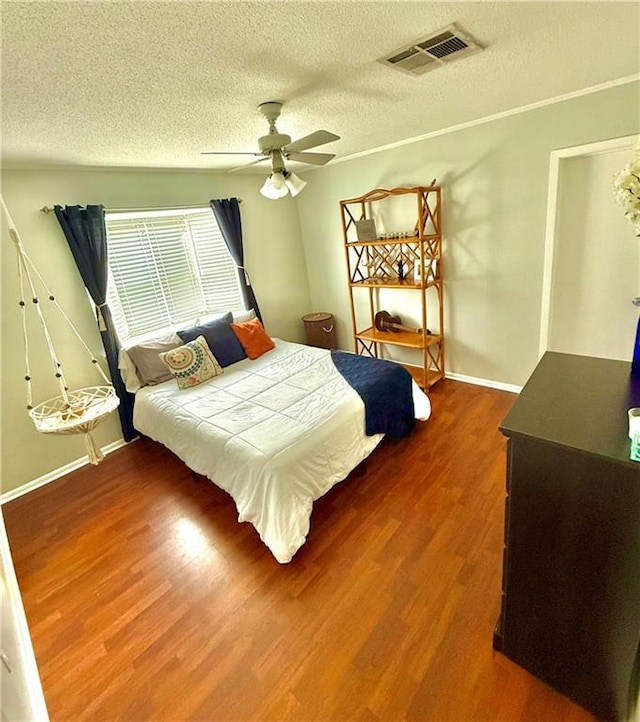 bedroom featuring visible vents, a textured ceiling, wood finished floors, baseboards, and ceiling fan